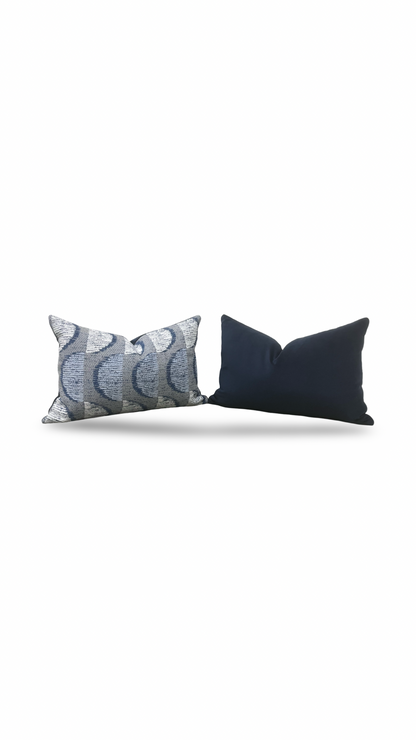 Two decorative pillows, one with a geometric pattern and the other solid dark color, on a white background.