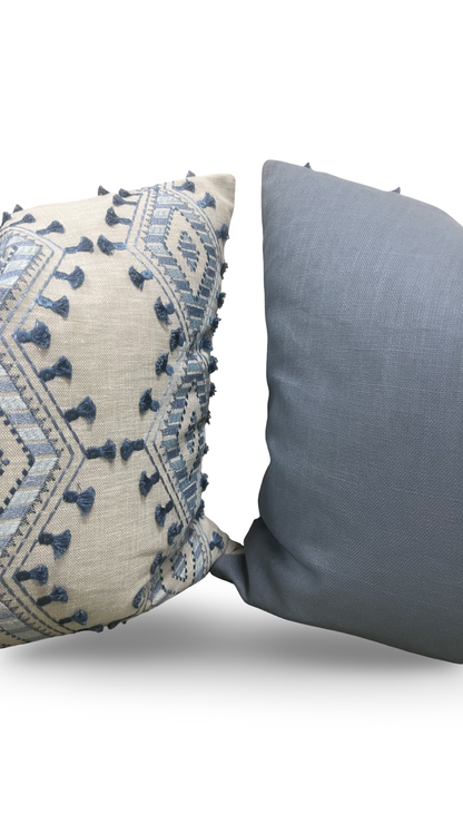 Two pillows, one with intricate blue patterns on a beige background and the other plain gray, on a white background.