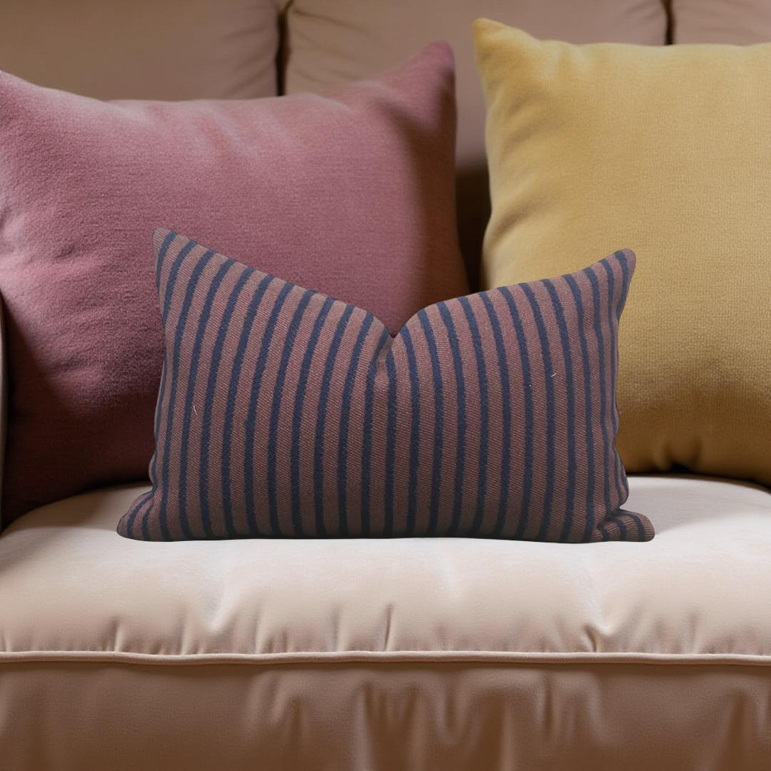 Three pillows in pink, yellow, and striped blue and purple on a beige couch.
