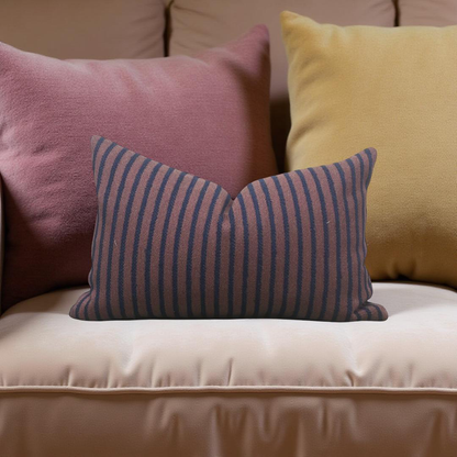 Three pillows in pink, yellow, and striped blue and purple on a beige couch.