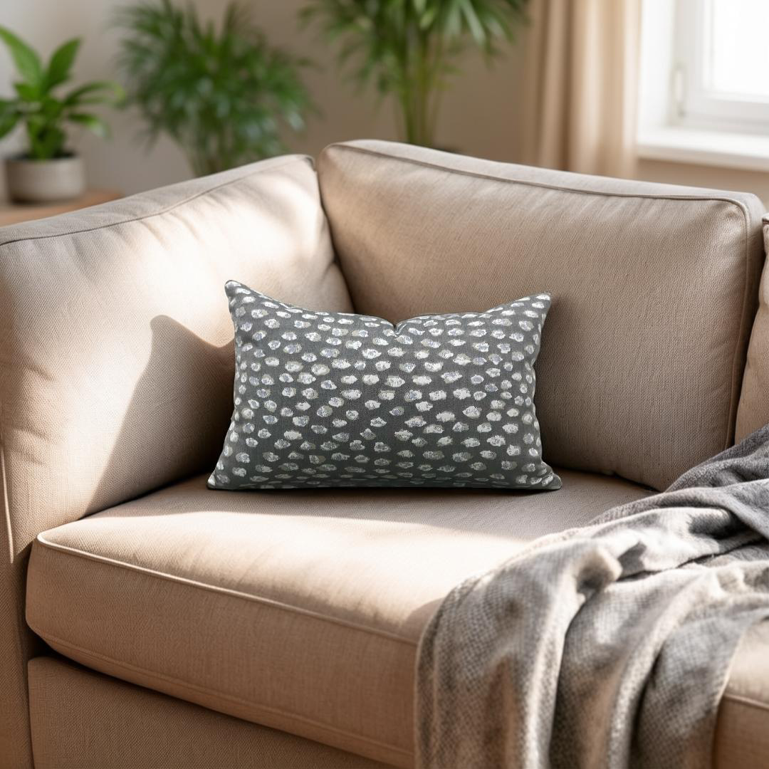 Beige sofa with a patterned gray pillow and blanket in a cozy living room.
