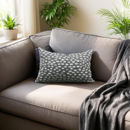 Gray sofa with decorative pillows and a blanket, surrounded by potted plants in a bright room.