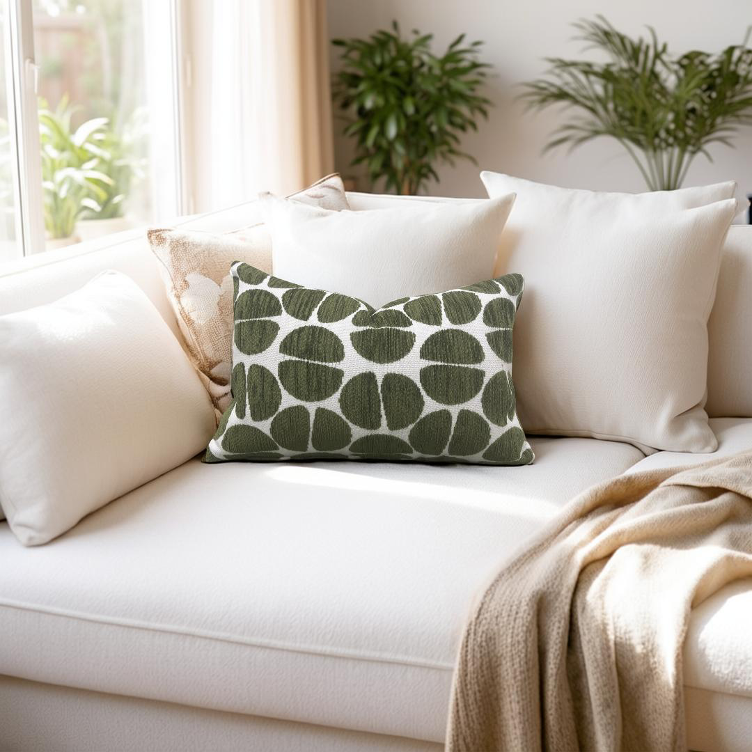 White sofa with green patterned pillow and beige blanket, plants in the background