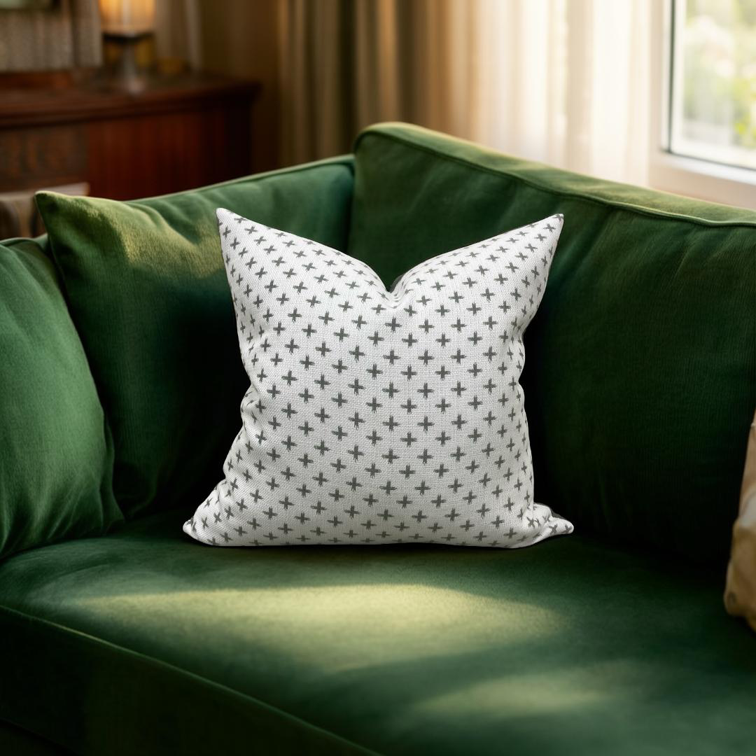 Green sofa with a white pillow featuring black cross patterns in a room with a window and curtain.