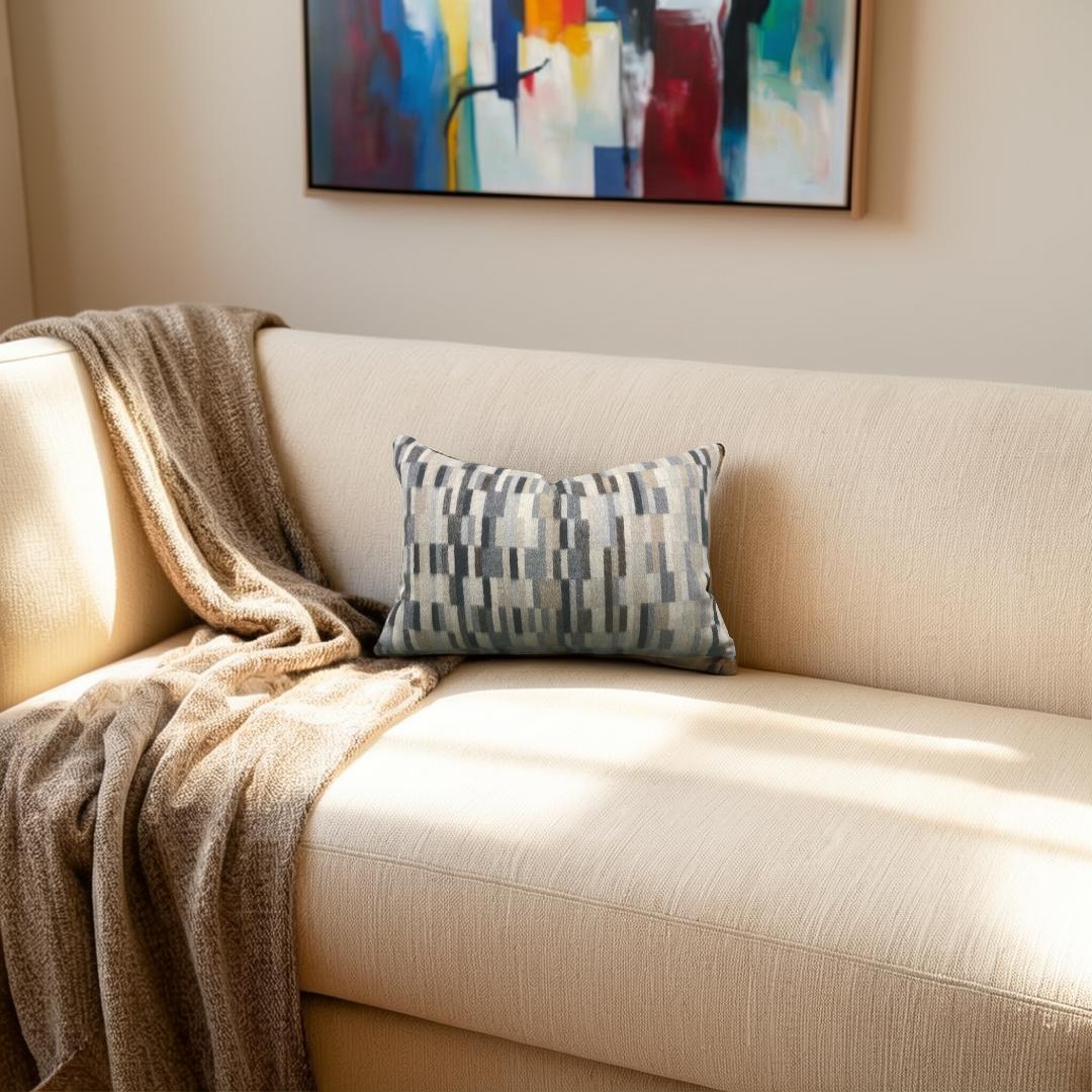 Beige sofa with a patterned pillow and a blanket, featuring a colorful abstract painting on the wall.