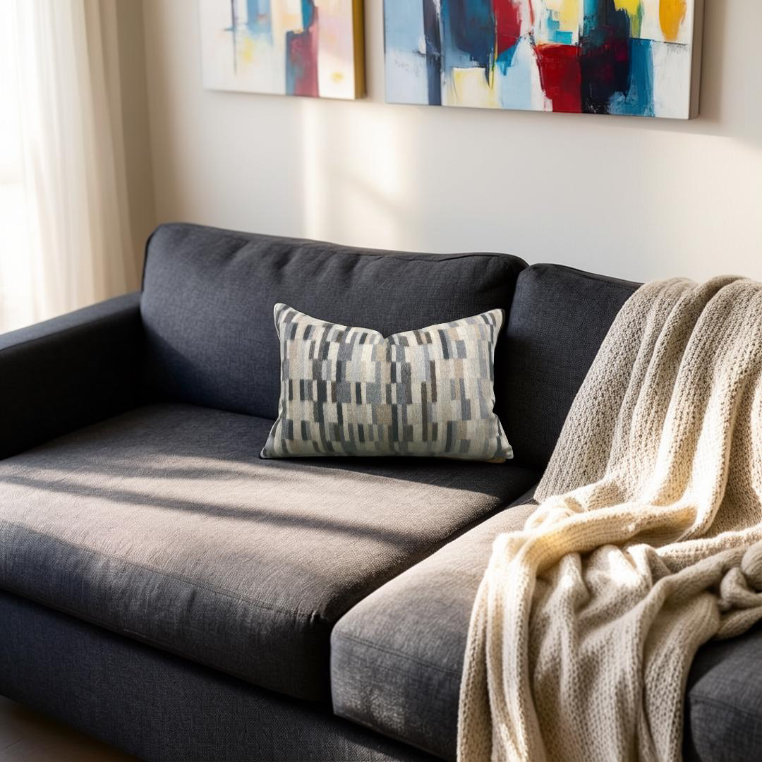 Gray sofa with a patterned pillow and beige blanket in a living room setting.