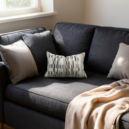 Gray sofa with cushions and a blanket in a room with a window.