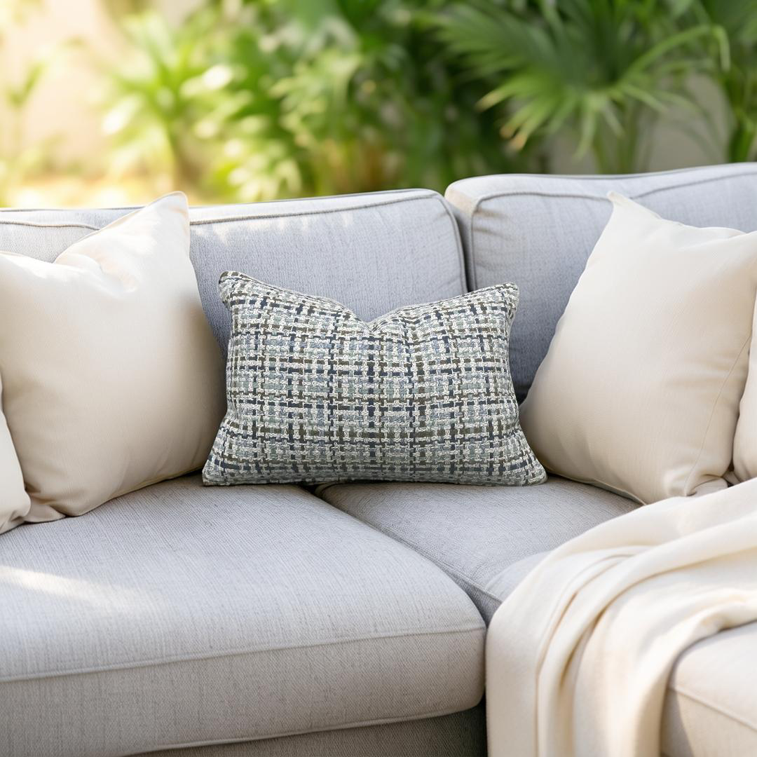 Gray sofa with decorative pillows and a blanket in an outdoor setting with greenery.
