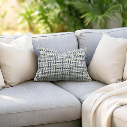 Gray sofa with decorative pillows and a blanket in an outdoor setting with greenery.